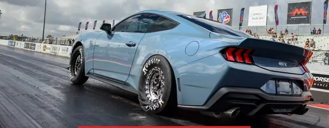 A modified Mustang launching off the drag strip start line