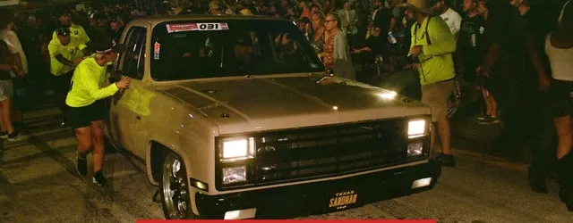 A Chevy C10 under lights with judges looking over it at night
