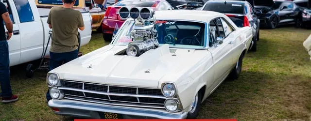 A white Ford Fairlane with a blown engine on the show car lawn